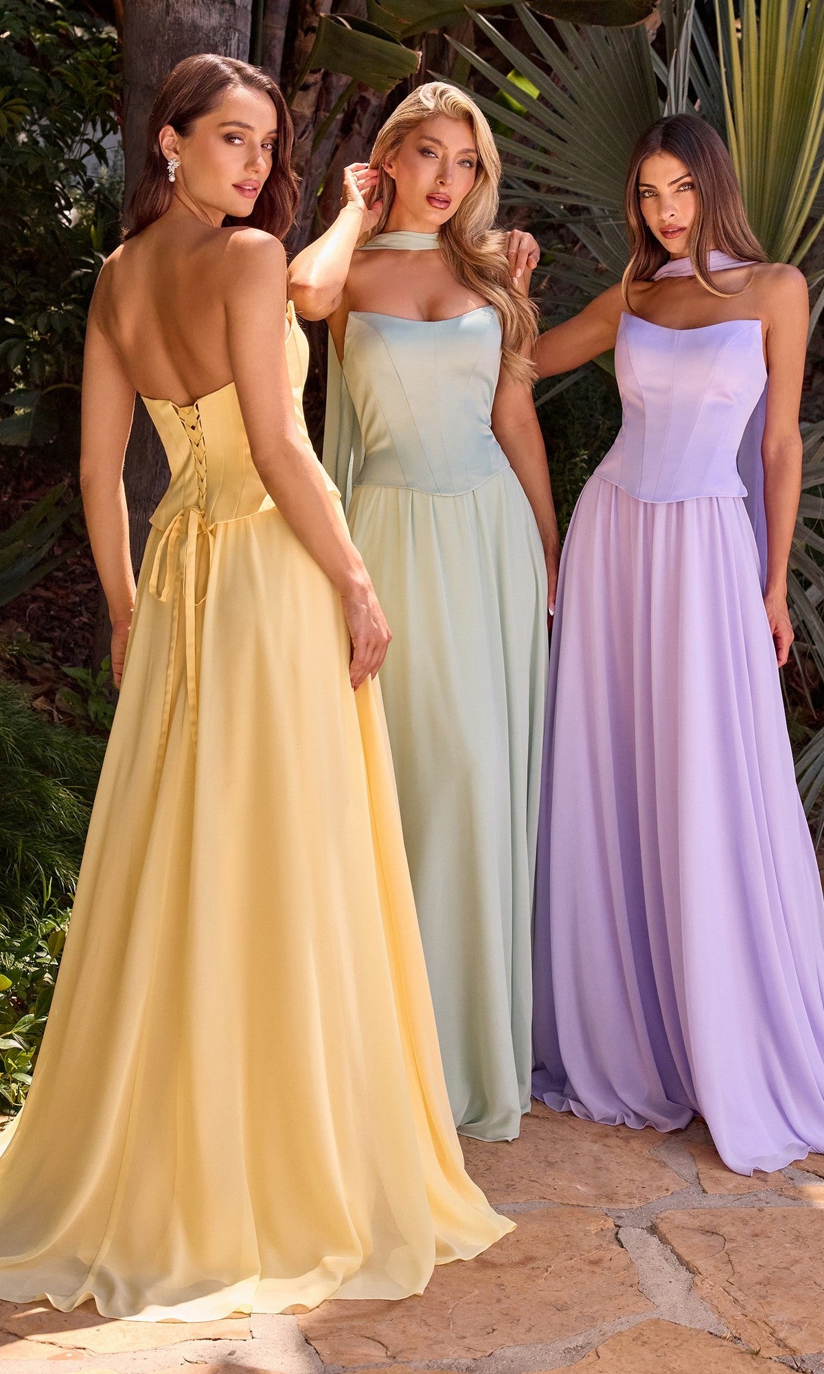 Three women stand outdoors in yellow, light blue, and lavender Strapless Long Corset Prom Dress: Ladivine CD386, with greenery in the background.